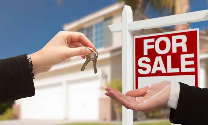 A person handing keys to another person in front of a house.