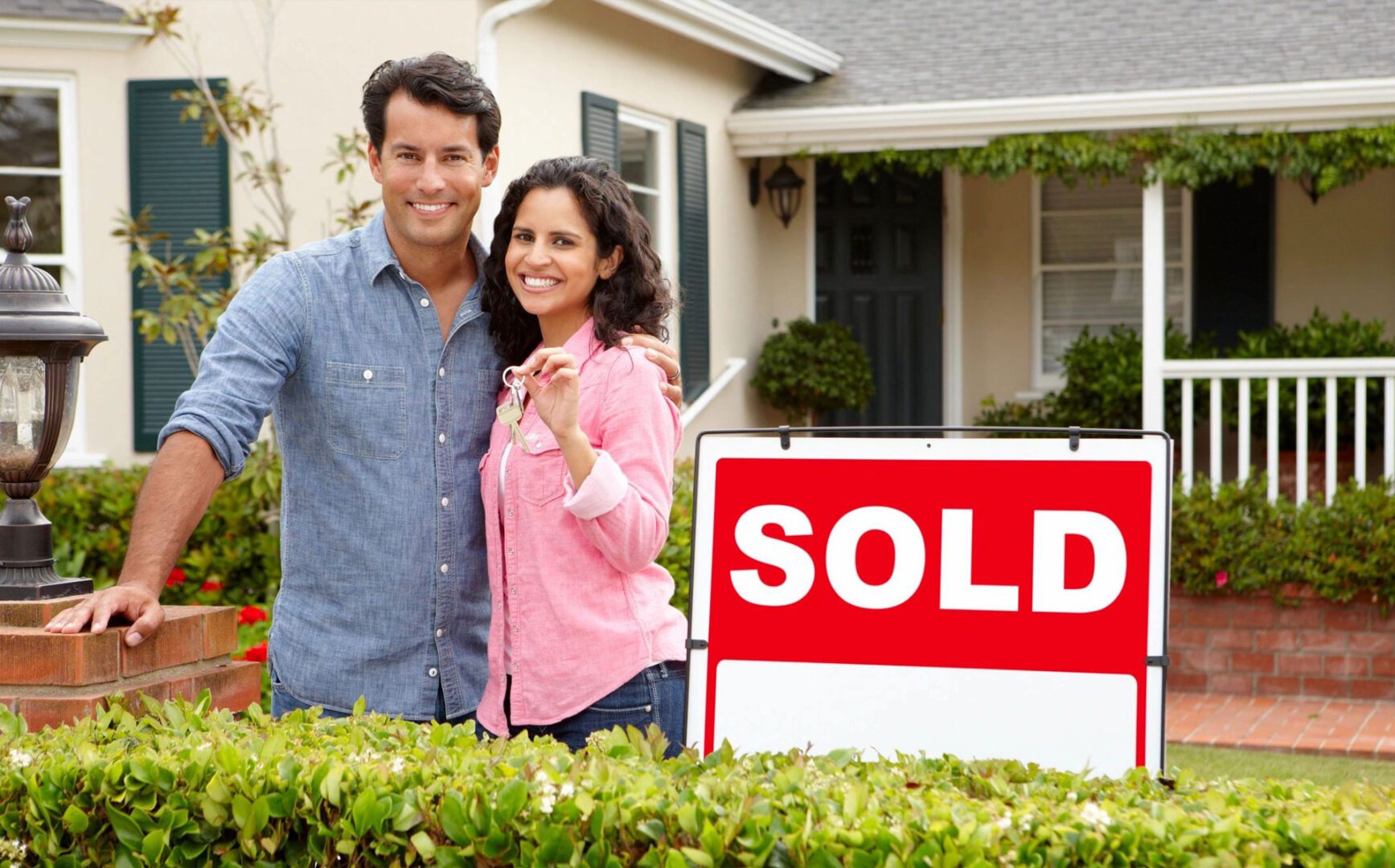 Happy couple outside home with sold sign